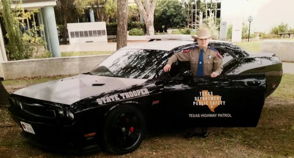 Young girl dressed as a Texas State Trooper beside a patrol car